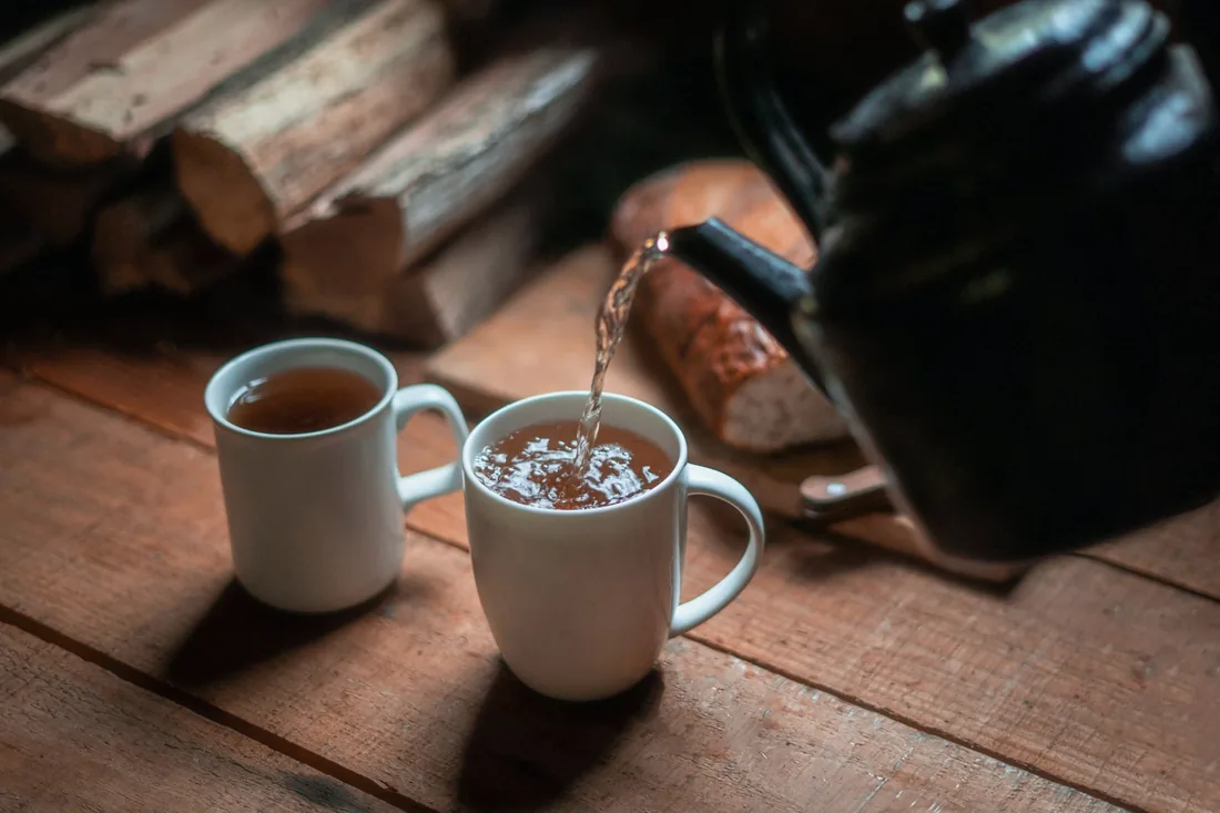 Une théière en céramique verse du thé dans deux tasses posées sur une table en bois