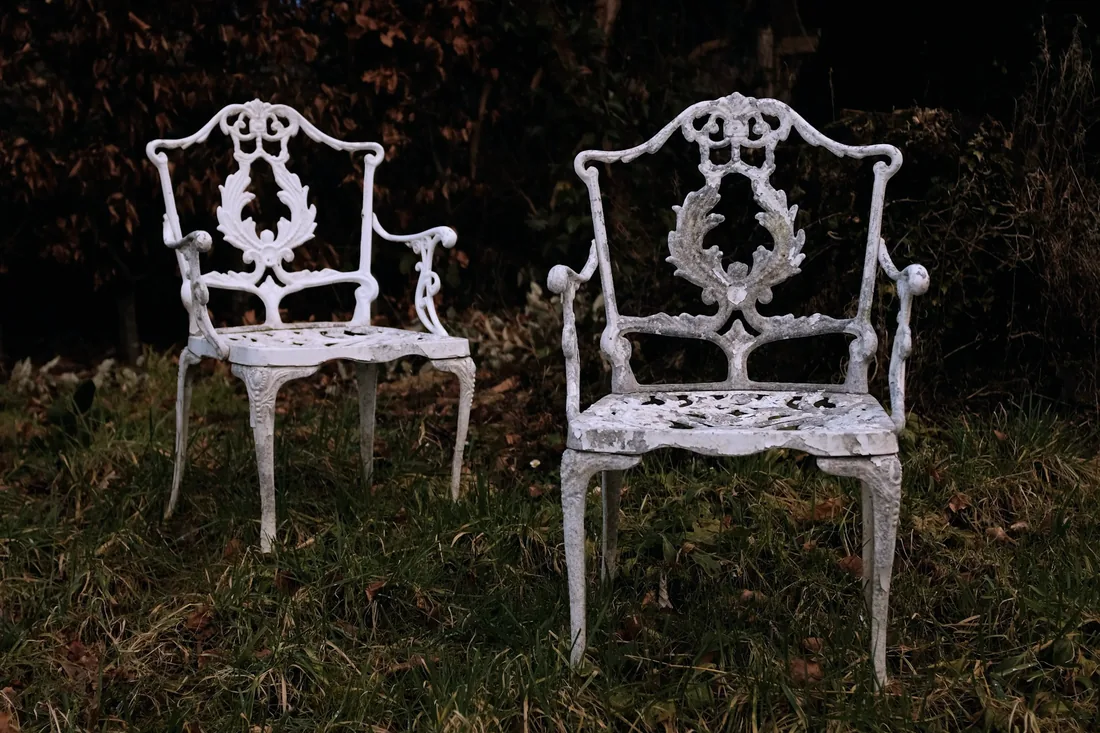 Deux fauteuils en fer blanc ouvragé posés face à face sur une pelouse sombre