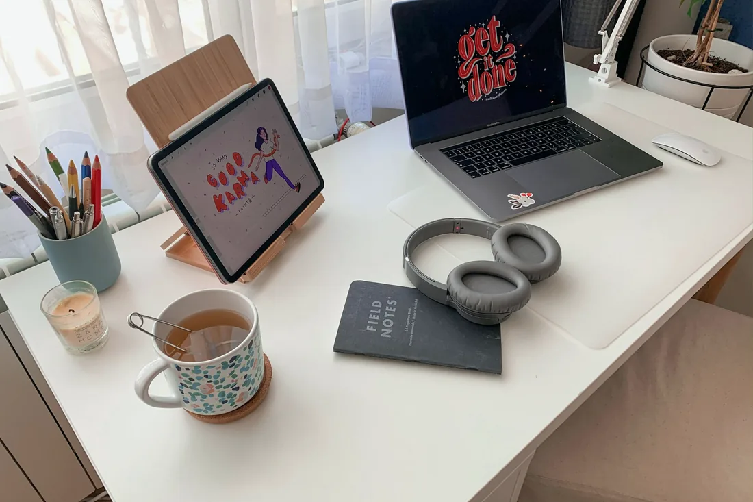 Un bureau blanc avec une tablette, un ordinateur, un casque et une tasse de thé