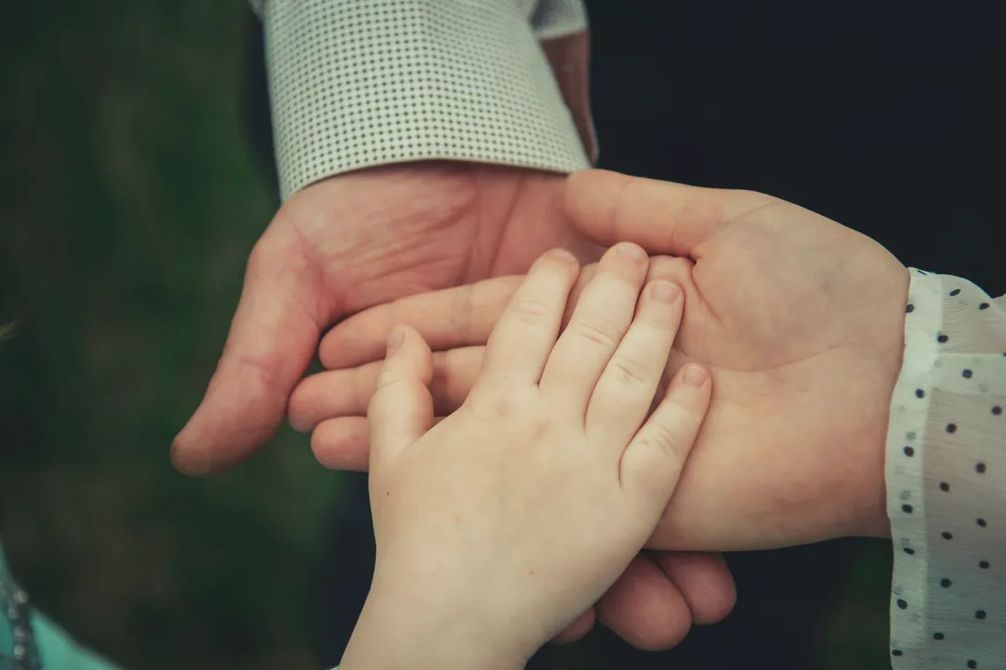 Les mains d'un adulte et d'un enfant posées l'une dans l'autre sur un fond sombre