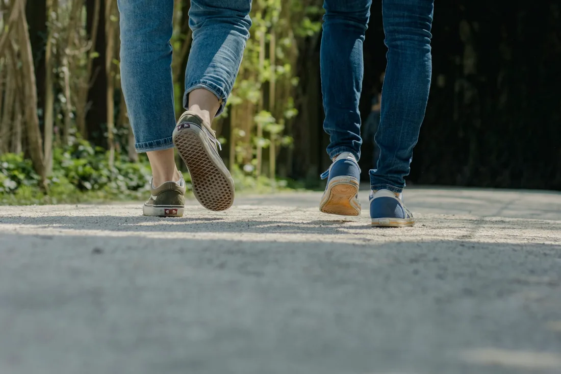 Les jambes de deux personnes en jean qui marchent côte à côte sur un chemin goudronné
