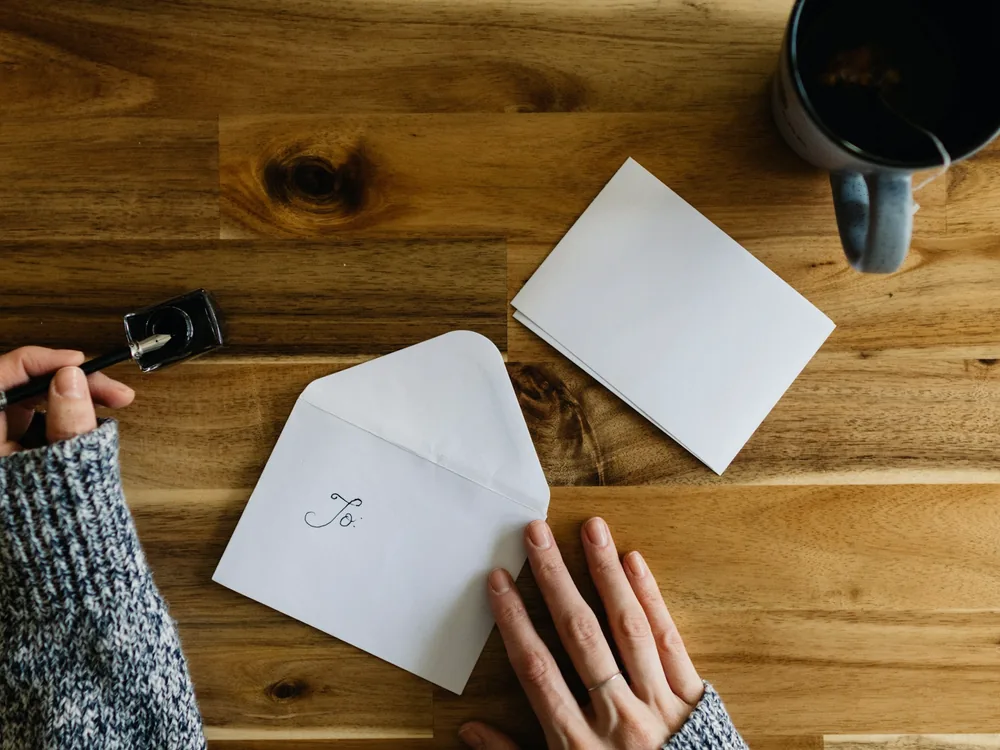 Deux mains qui ferment une enveloppe, un encrier et une tasse posés sur un plateau en bois