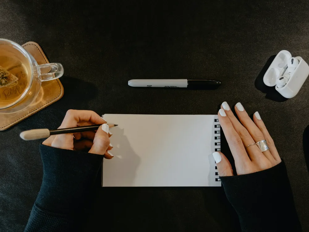 Un carnet ouvert, un stylo et une tasse de thé posés près d'une fenêtre lumineuse