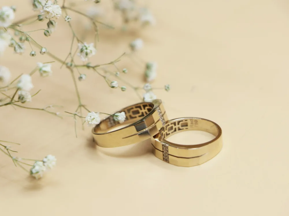 Deux alliances en or posées sur un fond crème, avec de petites fleurs blanches