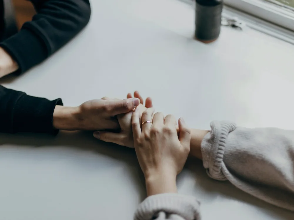Deux personnes assises face à face, les mains l'une près de l'autre sur une table claire