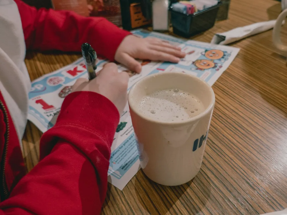 Les mains d'un enfant qui dessine à côté d'une grande tasse posée sur une table en bois